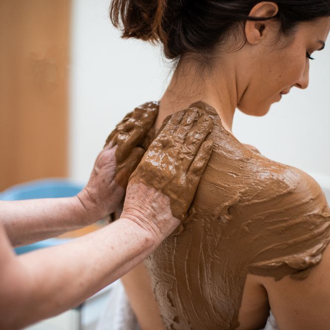 Bad Camberger Lehm wird auf dem Rücken einer Frau mit beiden Händen aufgetragen